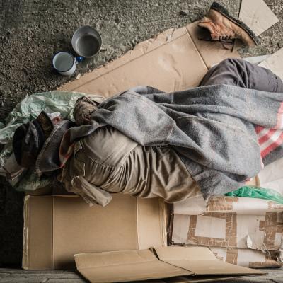 Man wearing sweater and blanket, sleeping on cardboard