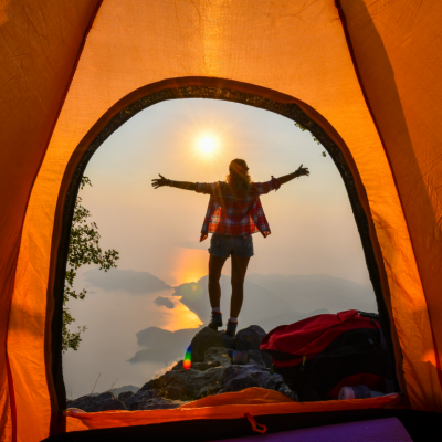 View from inside orange tent of woman camping and looking out at the mountains.