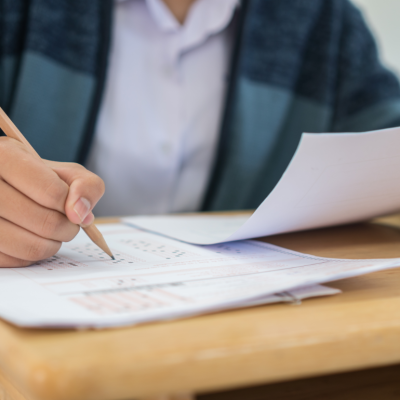 Closeup of student taking an exam at a desk, filling in an answer sheet with a pencil.
