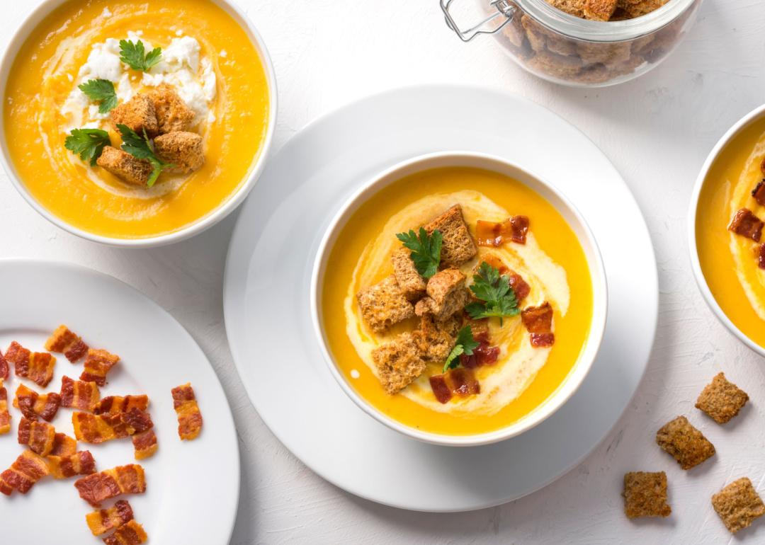 Top view of butternut squash cream soup with milk cream, bacon, croutons, feta cheese and parsley