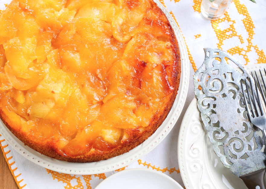 A gooey apple upside down cake on a white and orange towel with silver serving ware.