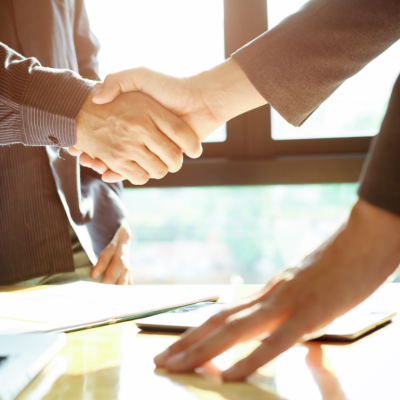 A handshake takes place over a desk and a laptop.