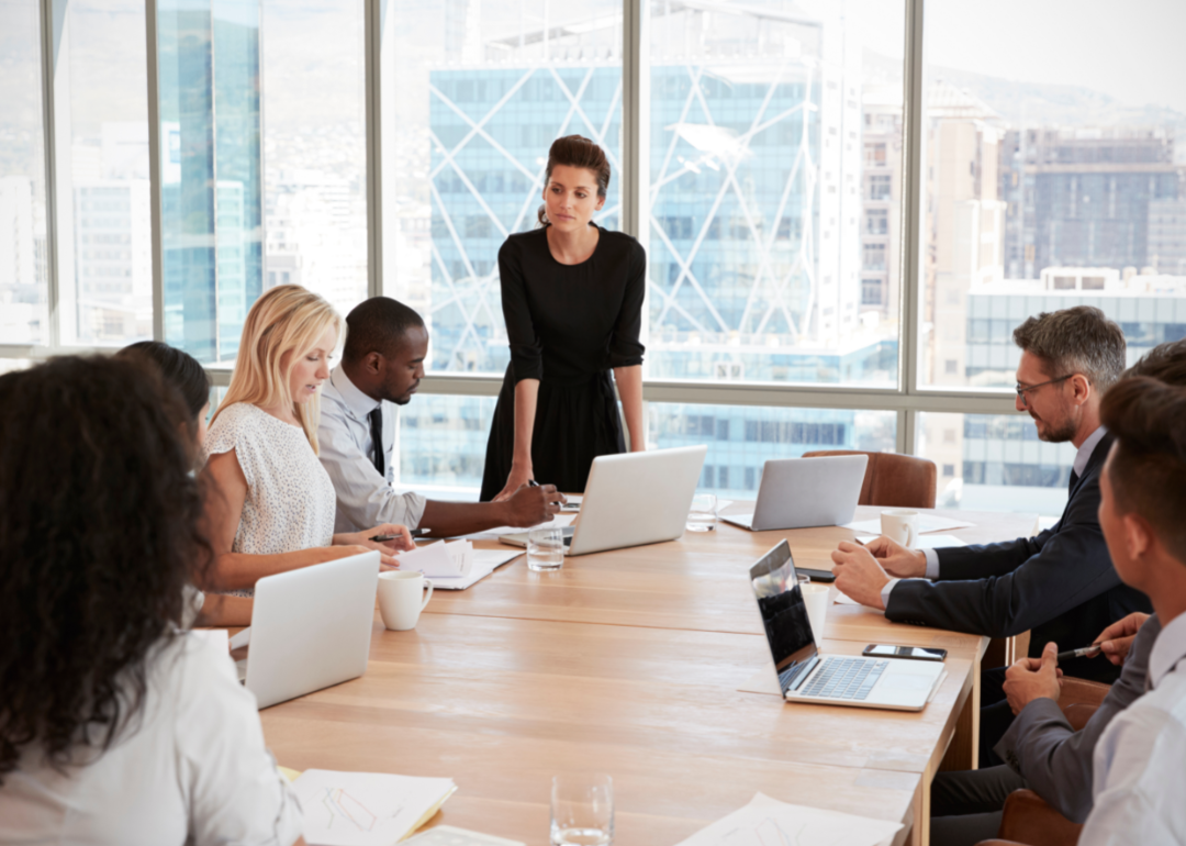 A woman in a conference room addressing a team of co-workers.