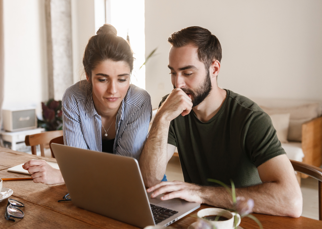 A couple concentrates on studying a document on a laptop in a living room.