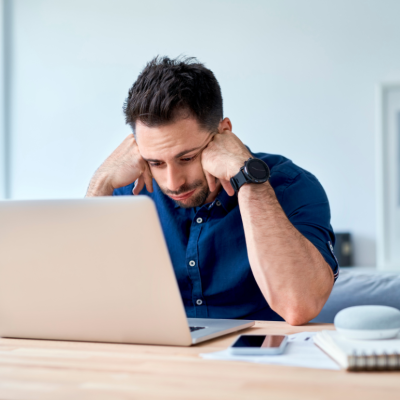 A young man sits at a desk and stares, discouraged, at a laptop