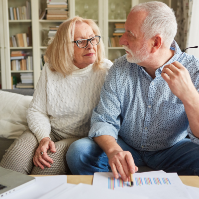 An older couple sit together on a couch going over financial paperwork.