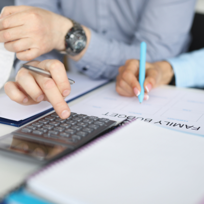 The hands of two people who are using a calculator and pen to make a family budget