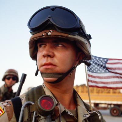A young U.S. marine arrives at Dhahran Air Base with the American flag flying behind him, during the Gulf War, in December 1990.