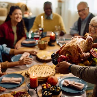 Person serving turkey to their extended family during a Thanksgiving meal.