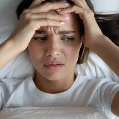 A person in bed holding their head after being awoken by a hypnic jerk.