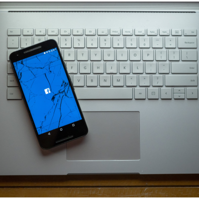 A cracked phone with the Facebook app loading sitting on a laptop.