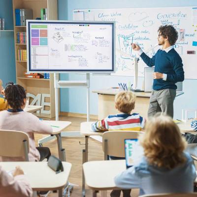 classroom from POV of students watching teacher at a screen in front