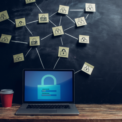 A laptop sitting on a desk beside a red cup of coffee; above the laptop are several post-its with locks drawn on them, connected by chalk lines to symbolize online security