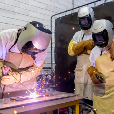 two college-age students watching their classmate practice welding
