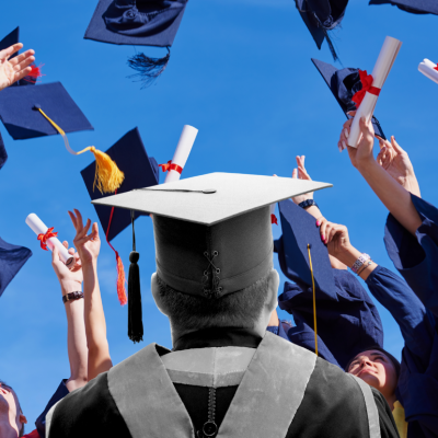Black and white image of a colege graduate against a colorful backdrop of graduates tossing caps into the air.