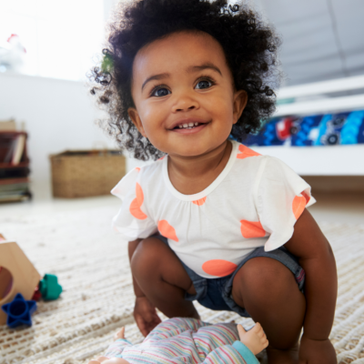 A happy baby wearing a polka dots plays with a baby doll.