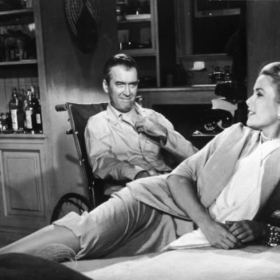 Grace Kelly (1929 - 1982) reclines on a bed while actor James Stewart (1908 - 1997) smiles at her from a wheelchair in a still from director Alfred Hitchcock's film, 'Rear Window,' 1954.
