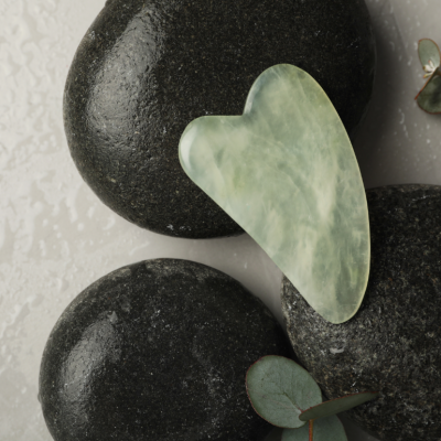 jade color gua sha tool displayed on black stones