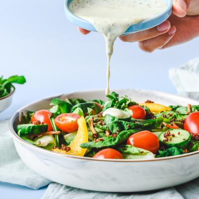 Pouring homemade creamy dressing on a garden salad with cucumbers and tomatoes.