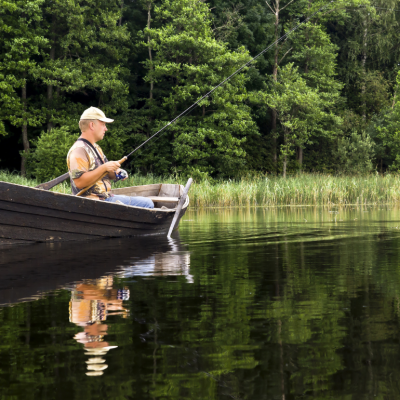 Fisherman sitting in the old, wooden rowboat and catching the fish on sunny day.