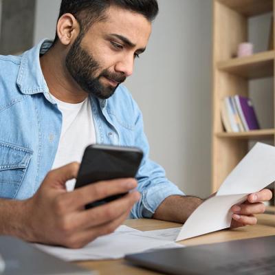 A college student seemingly calculating bills holding a phone with one hand and holding a paper bill with the other.