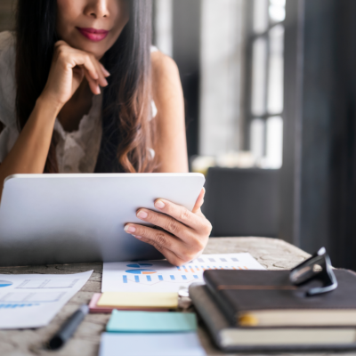 A woman seated at a desk considering investment options on a tablet.