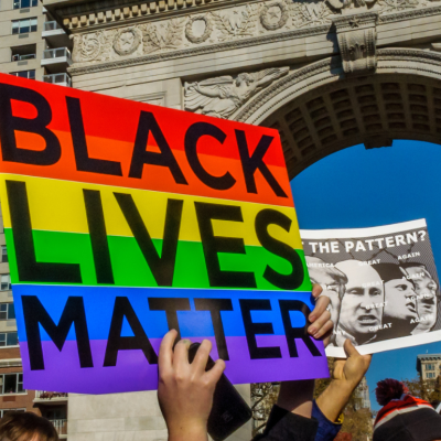 Student protesters from NYU holding up a sign that says "Black Live Matter" with a Pride flag in the background, in Washington Square Park, New York City