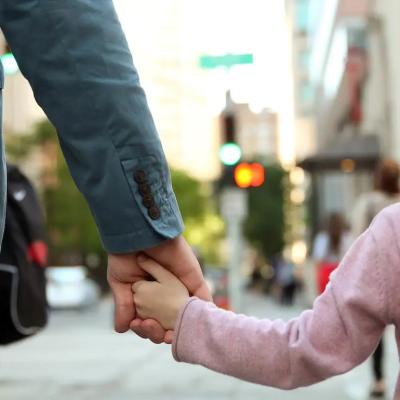 Adult holding child's hand waiting to cross a city street.
