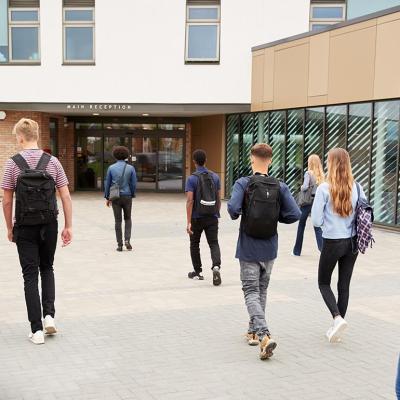 Eight students walking towards the main entrance of a school.