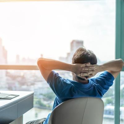 A student with laptop relaxing in a hotel room overlooking a skyscraper.