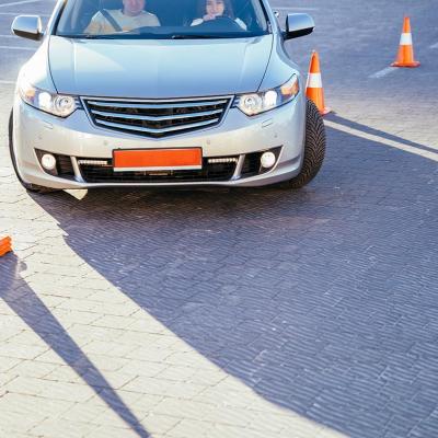 A young female student driver is being taught how to go around traffic cones.