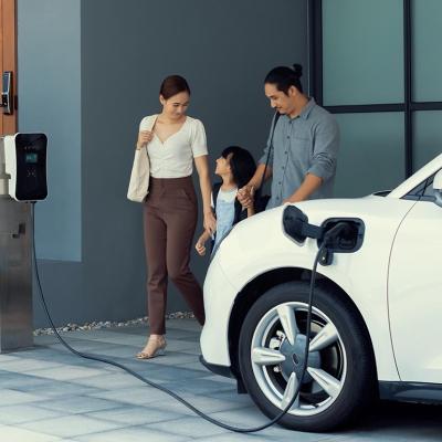 A family of three happily walking towards their electric car being charged in a station.