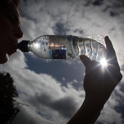 Silhouette of person drinking bottled water backlit by sun.