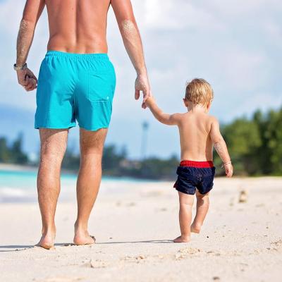 A dad and holding his toddler son's hand while they are walking on a white sand beach.