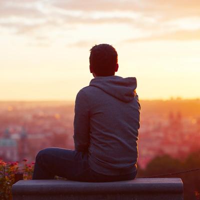 A man is sitting on a bench overlooking the city during sunset.