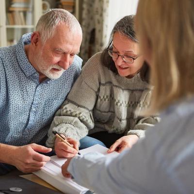 An elderly couple signing documents with a legal professional.