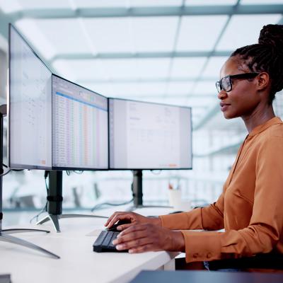 Accountant using three monitors to organize invoices using a software.