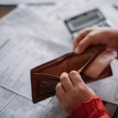 A woman's hands opening her empty wallet over a pile of power bills.