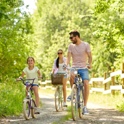 A family consisting of a father, mother and young daughter biking through a green wooded park