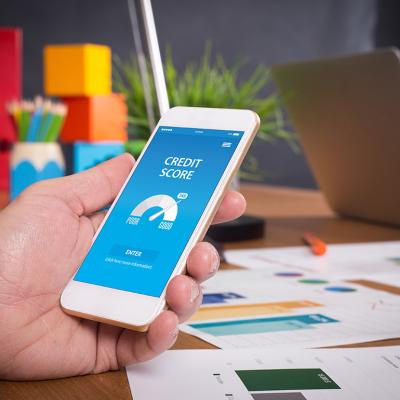 Employee in a workplace using a phone showing a credit score report.