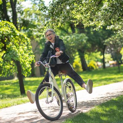 A middle aged woman happily having a stroll on a bike in a park.