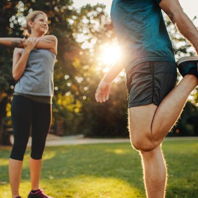 A man and a woman both stretching outdoors during a morning warmup.