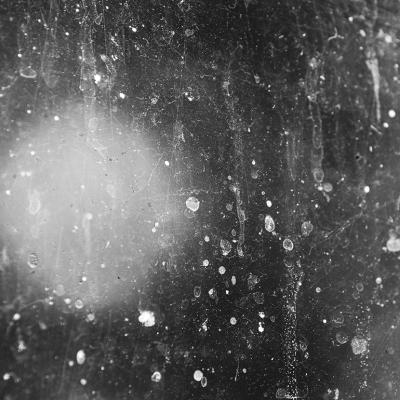 A detailed texture of hard water spots on a window in sunlight.