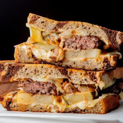 A patty melt consisting of a ground beef patty with melted cheese and topped with caramelized onions on two slices of griddled rye bread.