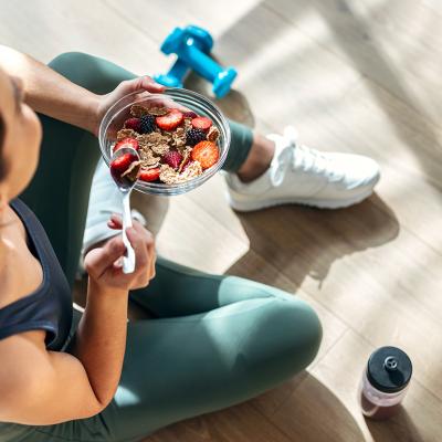 A young woman sitting on the floor post-workout and eating a bowl of oatmeal with fruits.