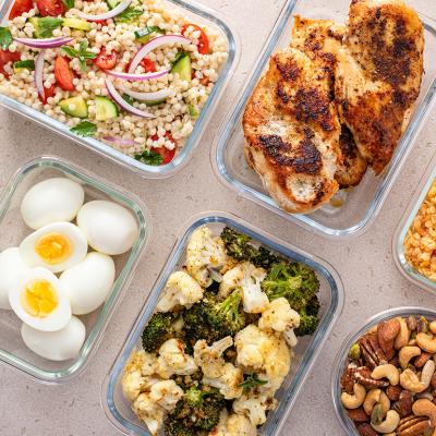 High protein meals such as roasted chicken breast, boiled eggs, various nuts and vegetables in meal prep containers.