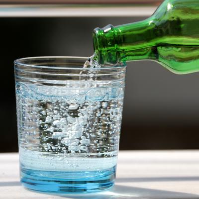 Sparkling water poured onto a glass from its bottle.