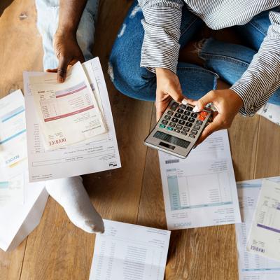 Two people on the floor managing debt by calculating invoices, bills and expenses.