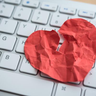 A red broken heart made out of paper on top of a computer keyboard depicting online dating scams.