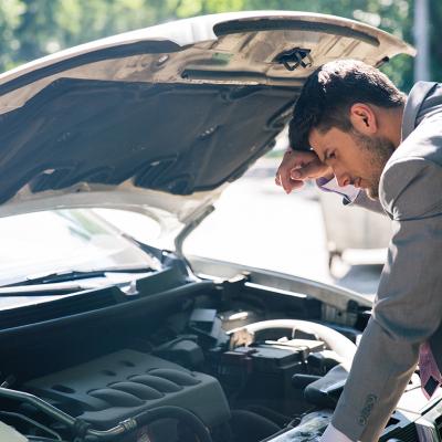 A car owner inspects his car's hood after it breaks down.